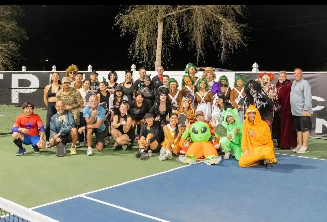 Around 45 players in costume posing on the courts at night under The Pickleball Universe banner