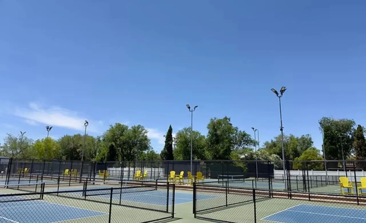 Outdoor pickleball courts at The Pickleball Universe: black fencing, court lights and yellow chairs under a clear Nevada sky